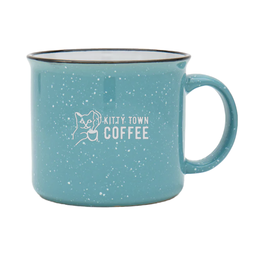 A teal ceramic mug with 'Kitty Town Coffee' logo engraved on it.
