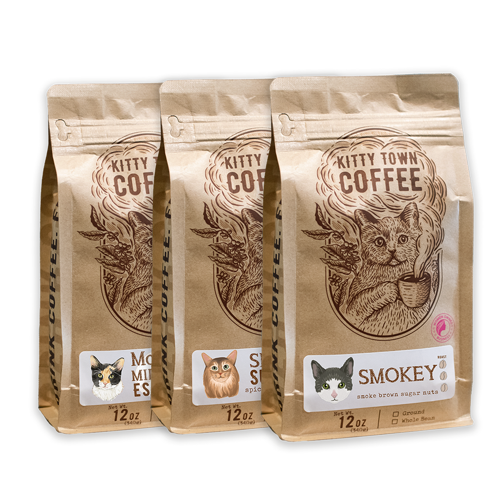Three bags of Kitty Town Coffee, with labels indicating the coffee names: Smokey, Simba's Sumatra, and Mooney's Midnight Espresso. Each bag is marked with a weight of 12 oz.