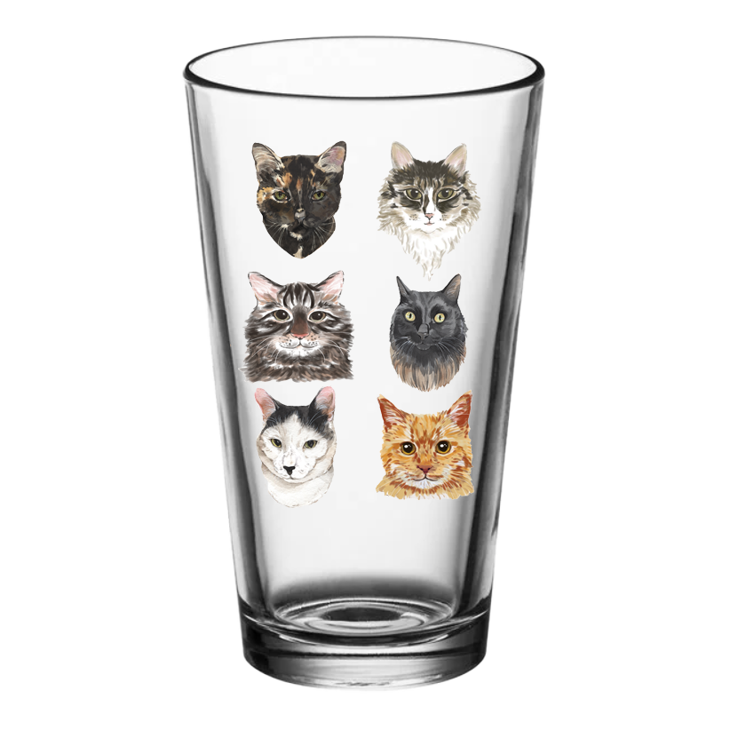 A clear pint glass with various cat faces printed on it.