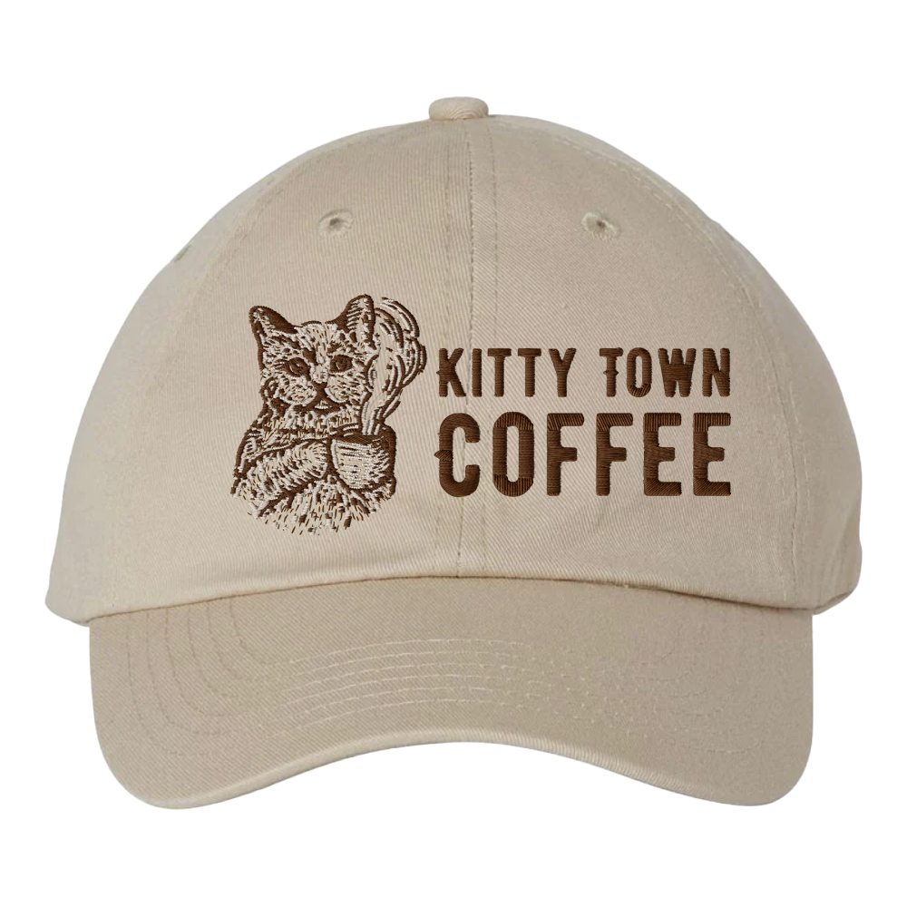 A beige colored cap with 'Kitty Town Coffee' printed on the front and an image of a cat holding a coffee cup.