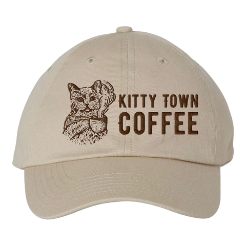 A beige colored cap with 'Kitty Town Coffee' printed on the front and an image of a cat holding a coffee cup.