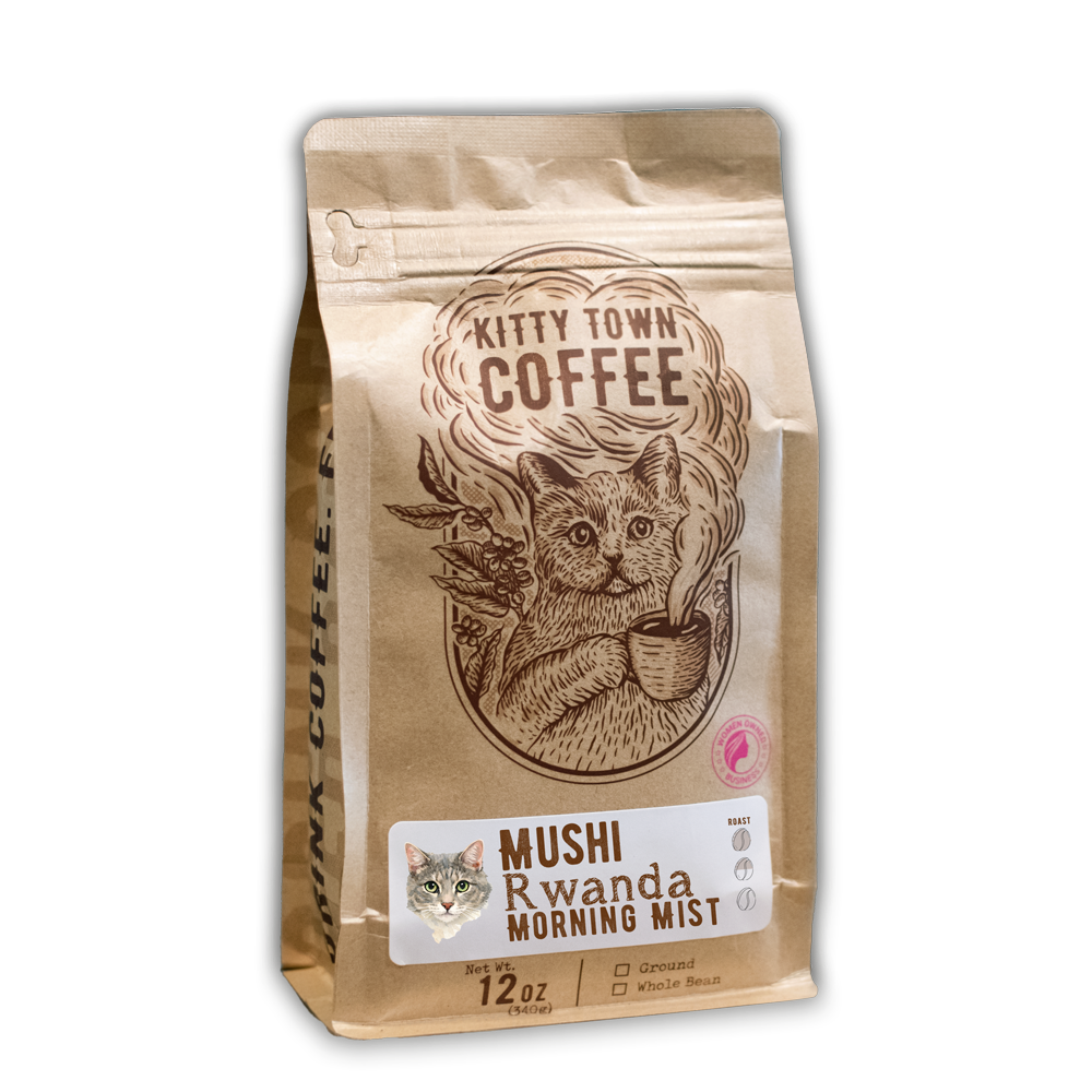 A 12 oz bag of Mushi Rwanda Morning Mist with the Kitty Town cat illustration and a photo of Mushi