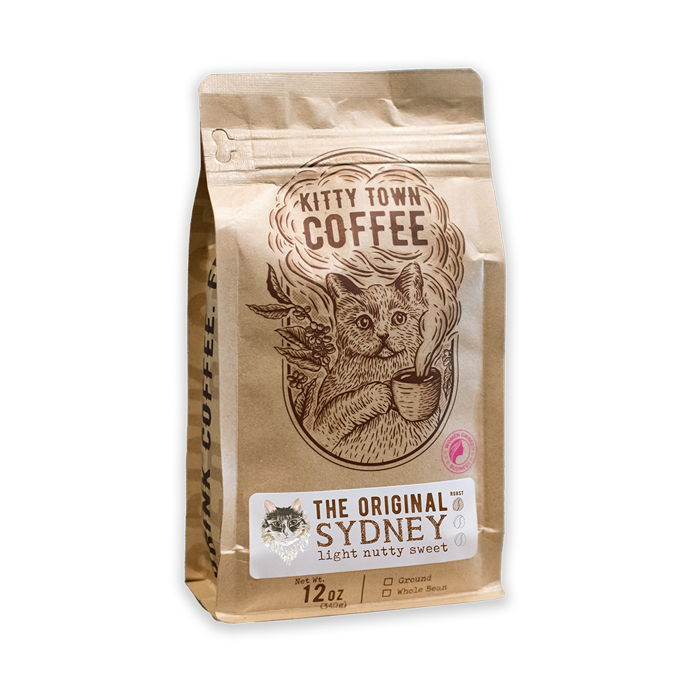 A packaged bag of Kitty Town Coffee, featuring 'The Original Sydney' light roast from Brazil. The bag is brown with an illustration of a cat and text detailing the coffee variety and roast level.