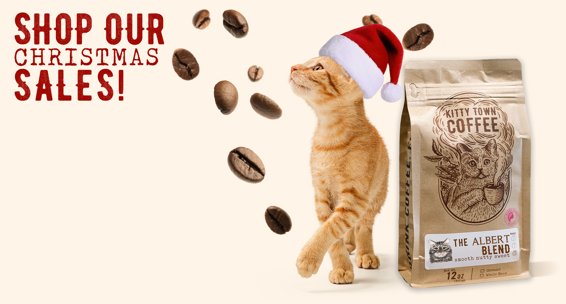 Cat wearing a Santa hat next to a bag of Kitty Town Coffee with coffee beans around on a white background.