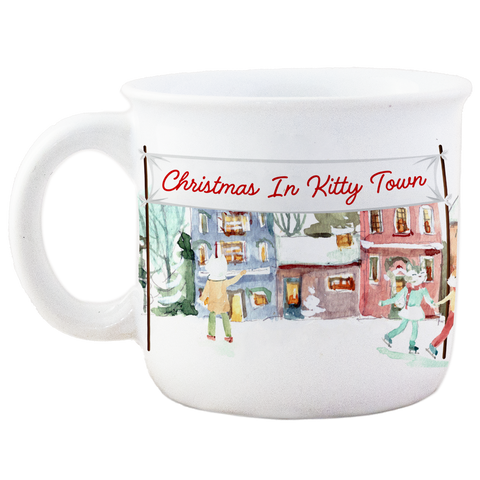 A white ceramic mug with a Christmas-themed illustration depicting cats in a town setting, and the text 'Christmas In Kitty Town'.