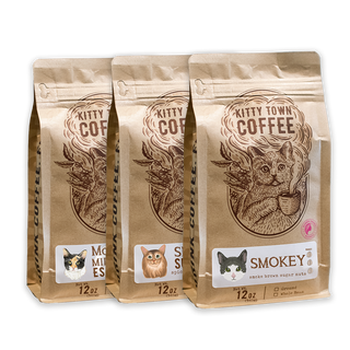 Three bags of Kitty Town Coffee, with labels indicating the coffee names: Smokey, Simba's Sumatra, and Mooney's Midnight Espresso. Each bag is marked with a weight of 12 oz.