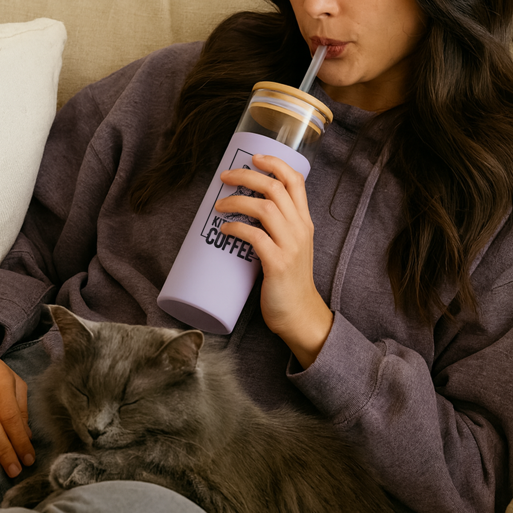 Person in a hoodie holding a purple tumbler with a straw, sitting on a couch with a cat next to them.