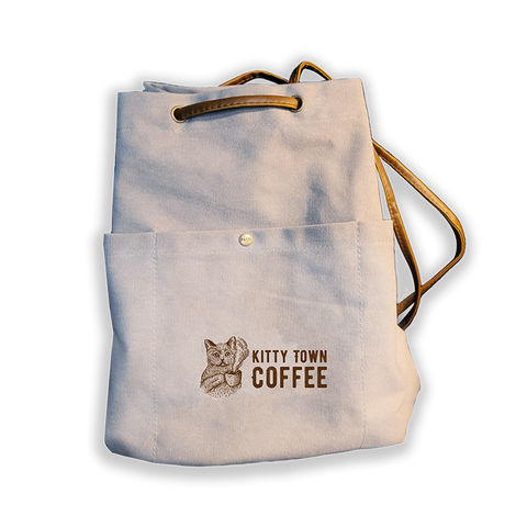 A large gray bucket style backpack with 'Kitty Town Coffee' printed on the front pocket and vegan leather straps.